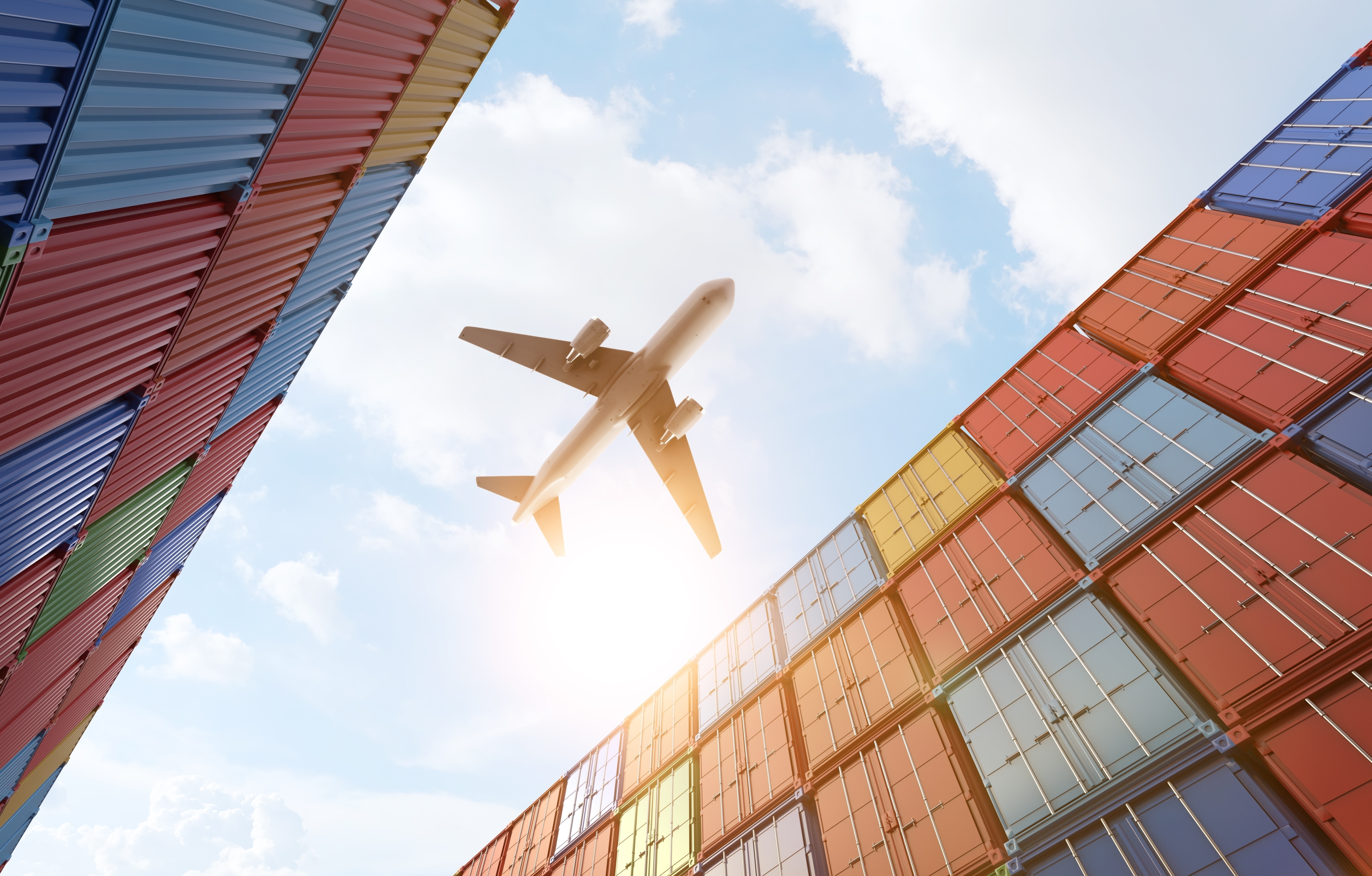 Cargo plane flying above stack of containers at container port